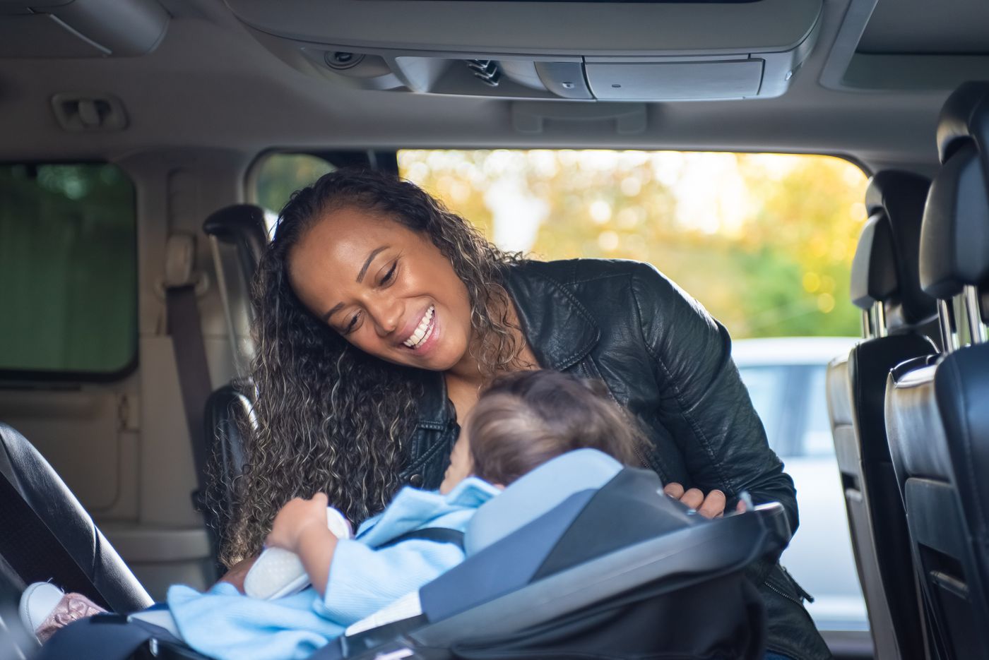 車のチャイルドシートに座る子どもと、隣で見守る母親